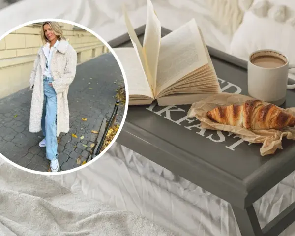 Kobieta w płaszczu z owczej wełny, symbolizującym quiet luxury, cieszy się śniadaniem w łóżku: książka, croissant i kawa.