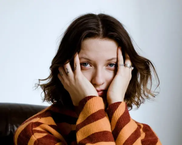 Justyna Święs Piernikowski w swetrze w pasy, z dłońmi przy twarzy, patrzy w obiektyw.