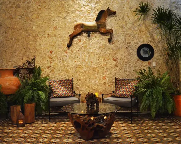 Un caballo decorativo adorna la pared de un patio exterior, complementado por plantas exuberantes y un rincón acogedor.