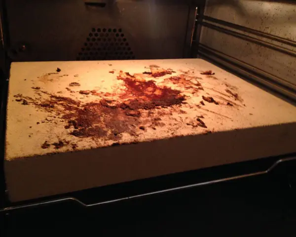 Ein schmutziger pizzastein mit braunen Flecken und Essensresten, der im Ofen liegt.