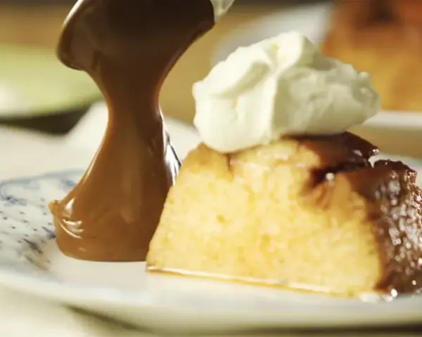 Un trozo de flan de 12 huevos, cubierto con caramelo y crema batida, servido en un plato con diseño azul.