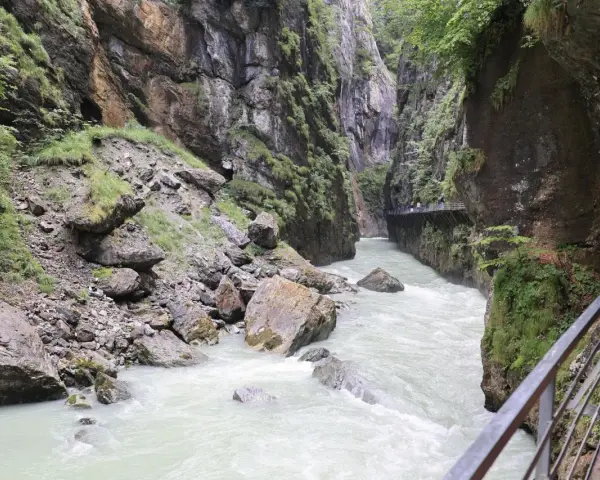 Aare Gorge, with its powerful river and dramatic cliffs, leads towards the Reichenbach Falls. A wooden walkway hugs the canyon wall.