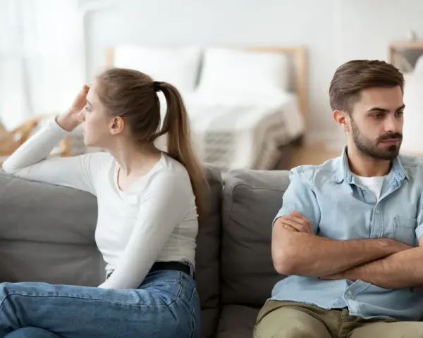 Couple marié, domicile différent, impôt. Ils sont assis sur un canapé, dos à dos, visiblement en désaccord.