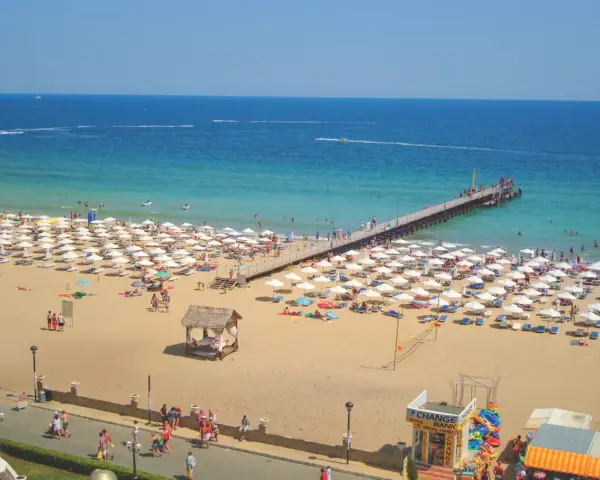 Słoneczny Brzeg, Bułgaria: tłumy plażowiczów, białe parasole, molo i turkusowe morze.