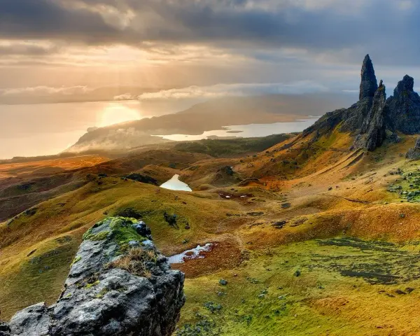 Paysage écossais spectaculaire, photo HDR. Des collines ondulantes aux teintes dorées et vertes, des lacs scintillants et des formations rocheuses imposantes sous un ciel dramatique.