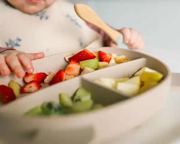 Bebé explorando fresas, kiwi y plátano en su plato. Es un buen momento para ofrecer fruta a los bebés.