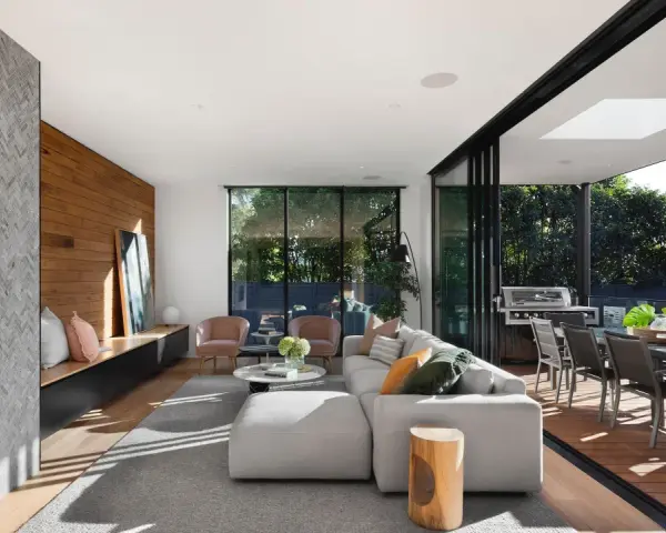Elegante salón con chimenea de piedra, pared de madera y grandes ventanales que conectan con una terraza. Un ejemplo de las últimas tendencias interiorismo.