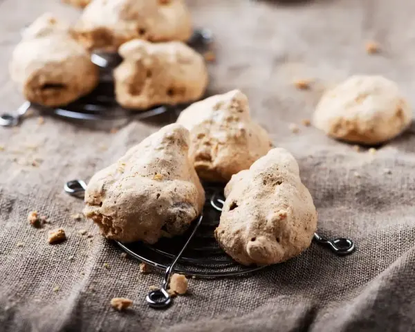 Biscotti meringati, dall'aspetto rustico, brutti ma buoni, su una griglia metallica e un telo grezzo.