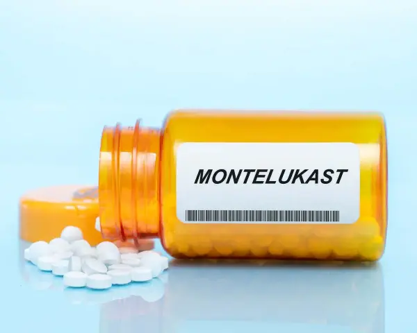 Pomarańczowa butelka leku MONTELUKAST, z której wysypały się białe tabletki.