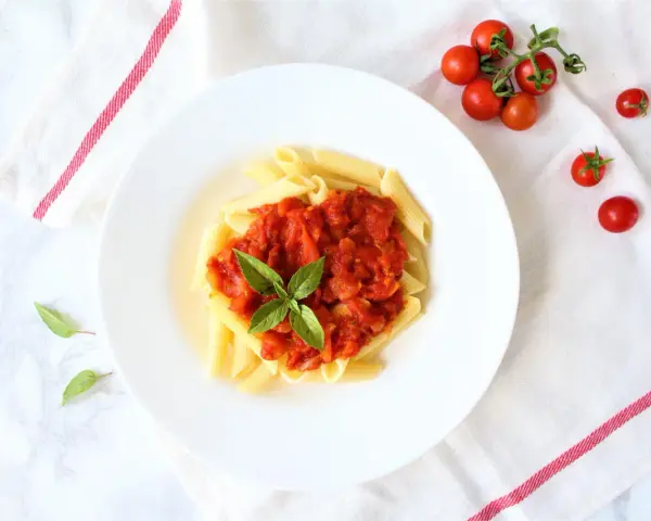 Penne z sosem pomidorowym i bazylią, obok świeże pomidorki koktajlowe.