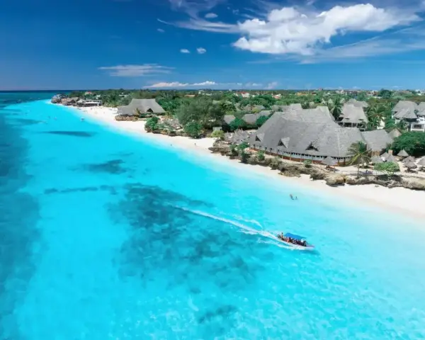 Zanzibar w lutym: idealna pogoda na rajskie wakacje. Turkusowa woda, biały piasek i łódź sunąca po oceanie.