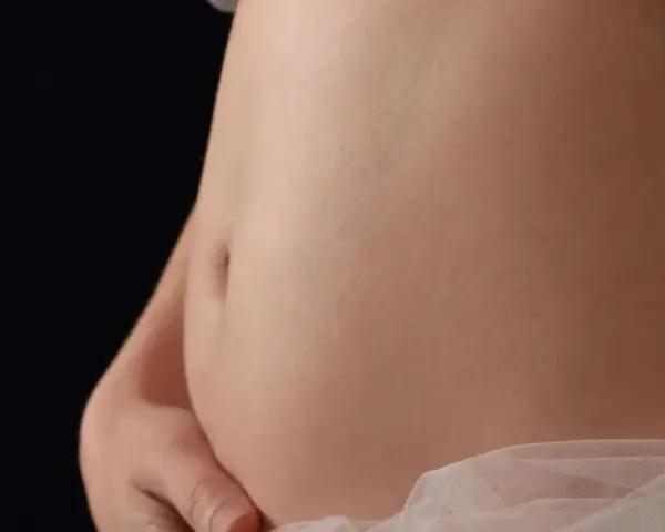 Pancia gonfia e dura, sembro incinta. La pelle liscia e chiara, con un leggero velo di tessuto rosa chiaro.