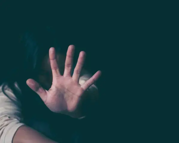 Frau hält Hand vor Gesicht, um sich vor psychischer Gewalt zu schützen. Sie fühlt sich bedroht, vielleicht wegen einer Wohnungszuweisung.