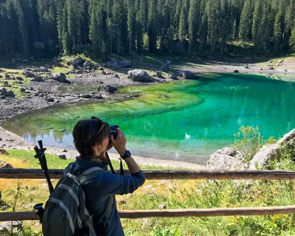 Donna con zaino e macchina fotografica cattura la bellezza del lago di Carezza, in Trentino Alto Adige.