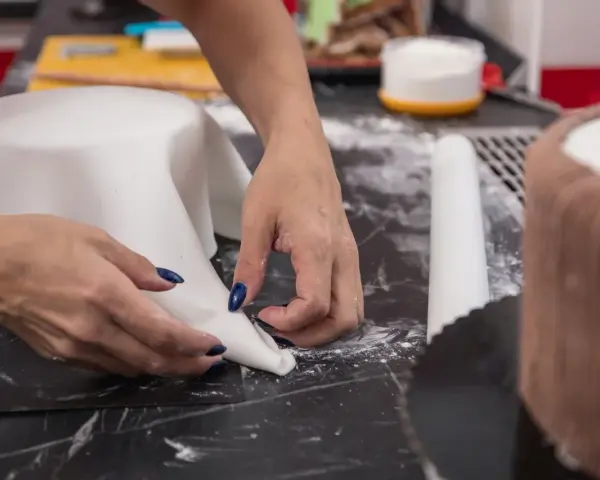 Hände formen weißen Fondant für eine Torte. Hier sind Tipps zum Fondant ausrollen für perfekte Ergebnisse.