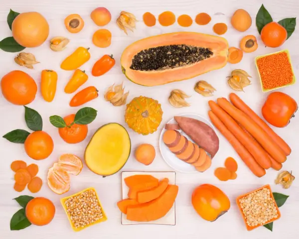Różnorodne pomarańczowe owoce i warzywa: papaja, marchew, bataty, pomarańcze, morele, kaki, dynia, papryczki.