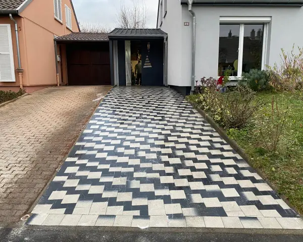Une allée en pavé au motif géométrique noir et blanc mène à une entrée de garage.