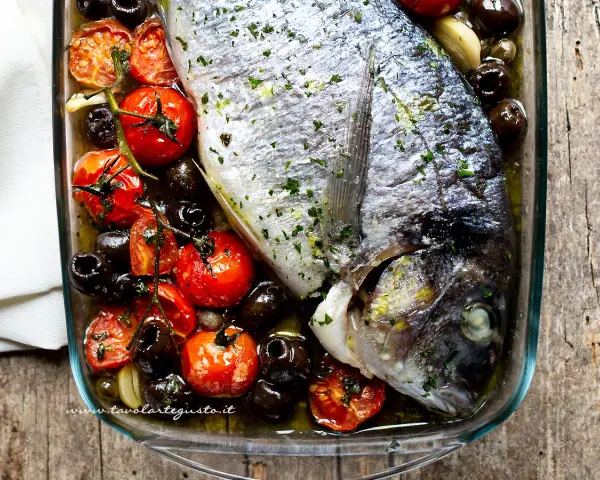 Filetti di orata al forno con pomodorini, olive nere e aglio, un piatto saporito e profumato.