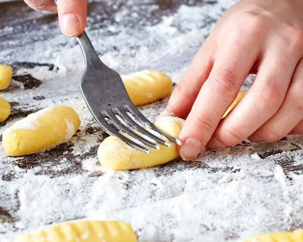 Hände formen mit einer Gabel die Rillen für original Gnocchi auf einer bemehlten Arbeitsfläche.