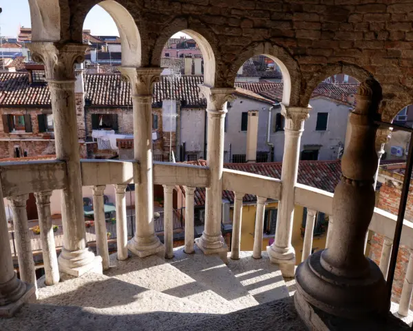 Dalla scala Contarini del Bovolo, vista sui tetti di Venezia. Colonne e archi in pietra creano un gioco d'ombre sulla gradinata.