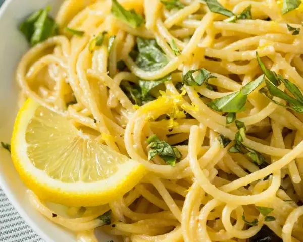 Un piatto invitante di spaghetti al limone, guarnito con scorza di limone e basilico fresco.