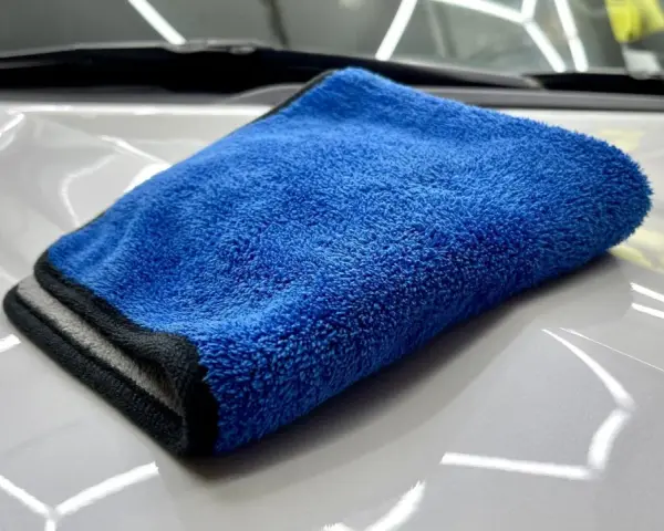 En blå torkhandduk ligger på en skinande vit bilhuv. Perfekt för att torka av bilen efter tvätt.