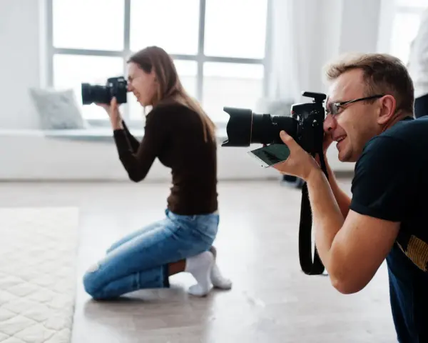 Dwóch fotografów klęczy i robi zdjęcia aparatem w jasnym studiu.