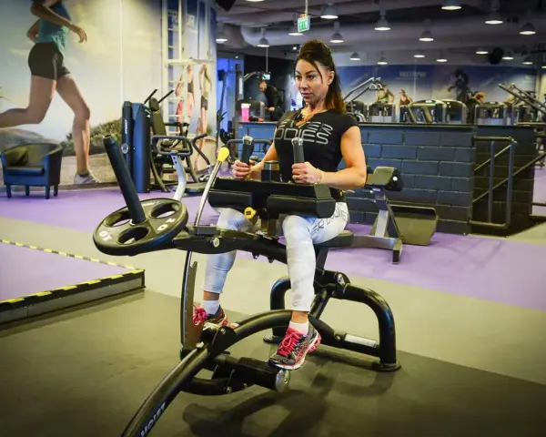 Kvinna tränar på gymmaskin. Hon har på sig träningskläder och fokuserar på sin träning. Hon verkar vara en seriös atlet som tar sin vad press på allvar.