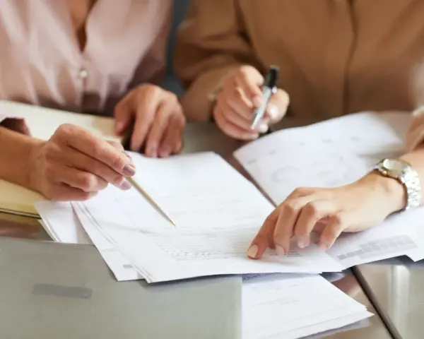 Dwie osoby analizują dokumenty, jedna wskazuje palcem na papier.