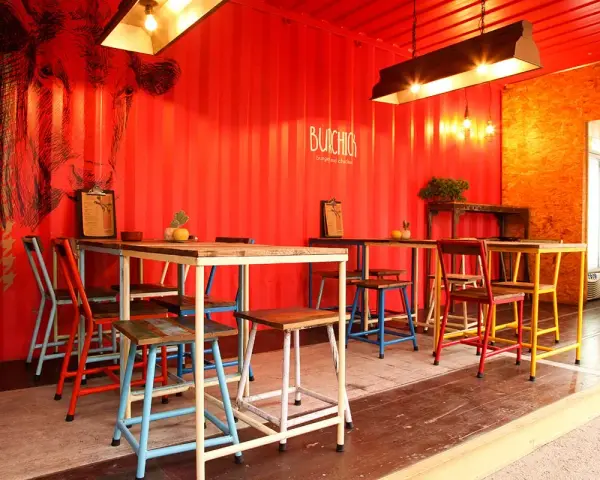 Decoración de restaurante con paredes rojas, mural de vaca y mesas coloridas.