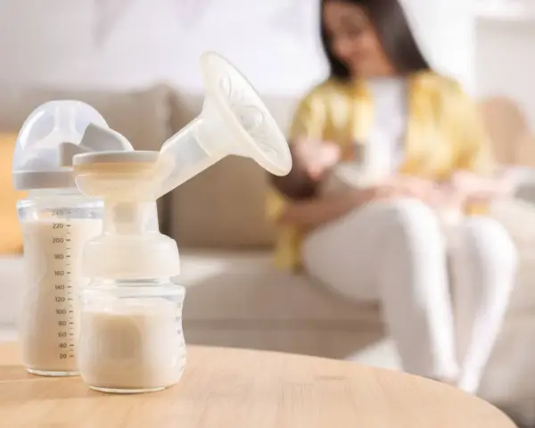 Biberon e tiralatte con latte materno, mentre una mamma allatta il suo bambino. Scopri come aumentare il latte materno in modo naturale.