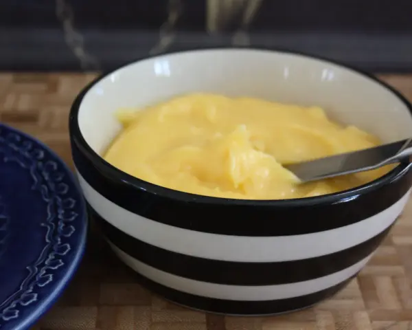 En skål med krämig, gul lemon curd, redo att bredas på en blå tallrik.