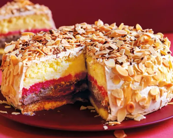 Una fetta di pizza dolce abruzzese, stratificata con crema, cioccolato e confettura, ricoperta di mandorle tostate e scaglie di cioccolato.