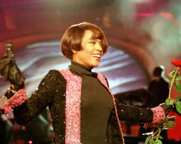 Whitney Houston z mikrofonem i czerwoną różą podczas niezapomnianego koncertu w Polsce.