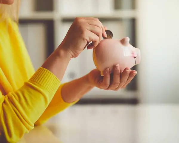 Persona con suéter amarillo deposita moneda en hucha. Un asesor fiscal te ayuda a ahorrar.