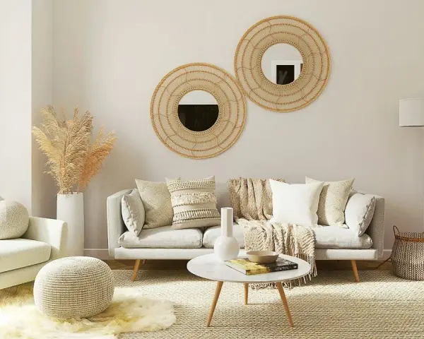 Przytulny salon w stylu scandi chic: jasna sofa, fotel, okrągłe lustra z plecionki, dywan i dekoracje z trawy pampasowej.