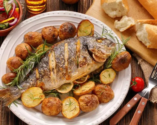 Pieczona ryba z ziemniakami, cytryną i rozmarynem na talerzu.