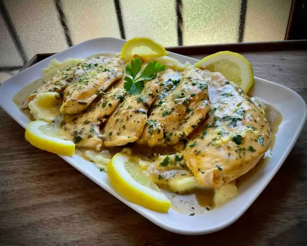 Delicioso pollo al limón con puré de patatas, adornado con perejil fresco y rodajas de limón.