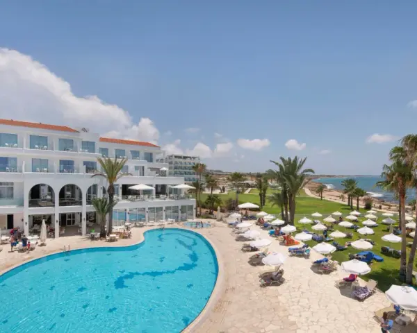 Słoneczny dzień w Akti Beach Village Resort. Basen, leżaki, palmy i morze - idealne miejsce na wakacje.