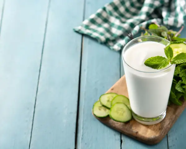 Szklanka białego napoju, idealna na kefir w ciąży, ozdobiona plasterkami ogórka i miętą.