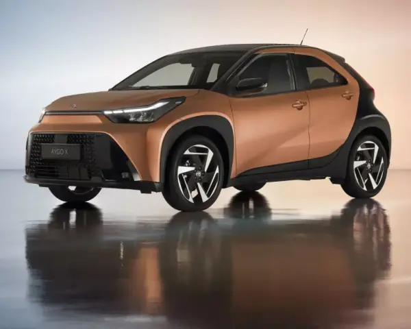 Brązowy Toyota Aygo X z czarnym dachem i felgami na błyszczącym podłożu.