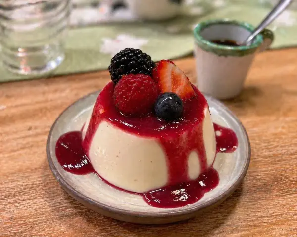 Cremige Panna Cotta mit Beeren und rotem Fruchtsirup auf einem Teller.