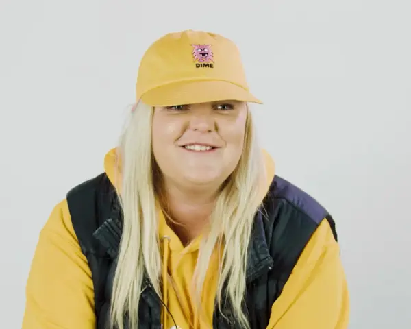 Frau mit gelber Kappe und Kapuzenpullover lächelt.