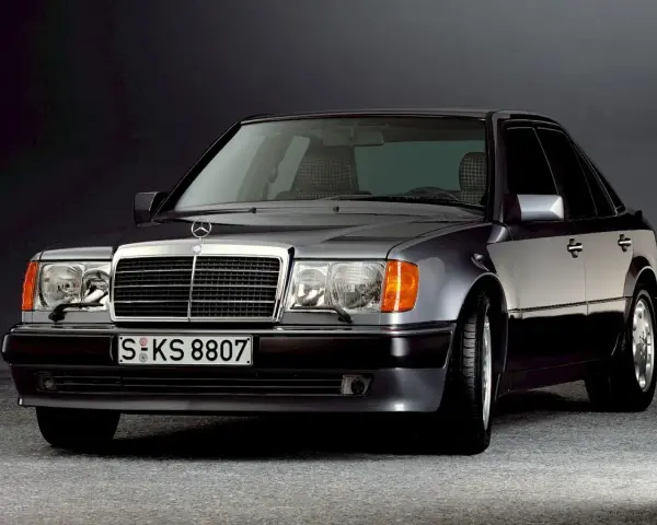 Klasyczny Mercedes W124 w ciemnym kolorze, z charakterystyczną atrapą chłodnicy i reflektorami. Ten model słynie z niezawodnych silników.