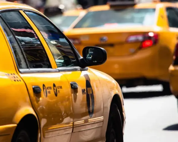 Gelbe Taxis in den USA, ein ikonischer Anblick. Die Spiegelung der US-Flagge im Fenster des vorderen Taxis.