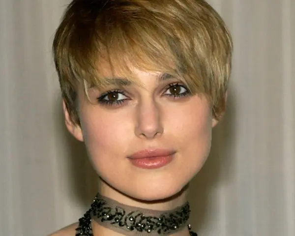 Primo piano di una donna con capelli biondi e tagli corti belli, trucco occhi marcato e un choker decorato.