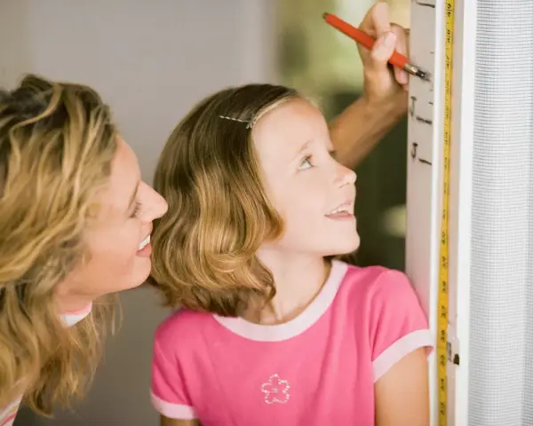 Mama mierzy córkę, która z zaciekawieniem patrzy na miarkę. Czyżby zastanawiała się, dlaczego dziecko nie rośnie tak szybko, jak by chciała?