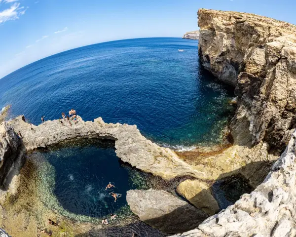 Ludzie kąpią się w naturalnym basenie skalnym, znanym jako blue hole, otoczonym klifami i turkusowym morzem.