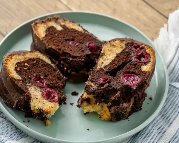 Saftiger Marmorkuchen mit Kirschen, überzogen mit Schokolade, auf einem Teller angerichtet.
