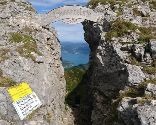 Himmelspforte am Schafberg: Ein Felsentor mit Holzinschrift, das den Blick auf einen See freigibt. Ein Wanderer steht im Durchgang.